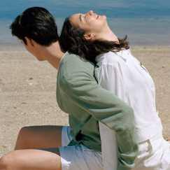 Man and woman sitting back to back on the beach, laughing